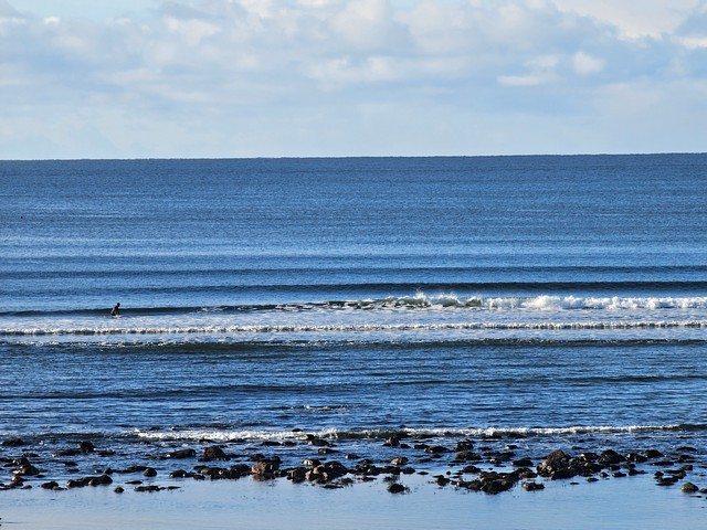 Small waves breaking in front of the shop as a longboarder makes their way deeper